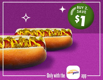 Two Jumbo Hot Dogs in buns with toppings and condiments with a green holiday ornament. Only with the A M P M app.